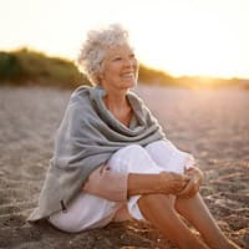 Senior woman sitting peacefully on the beach during sunset.