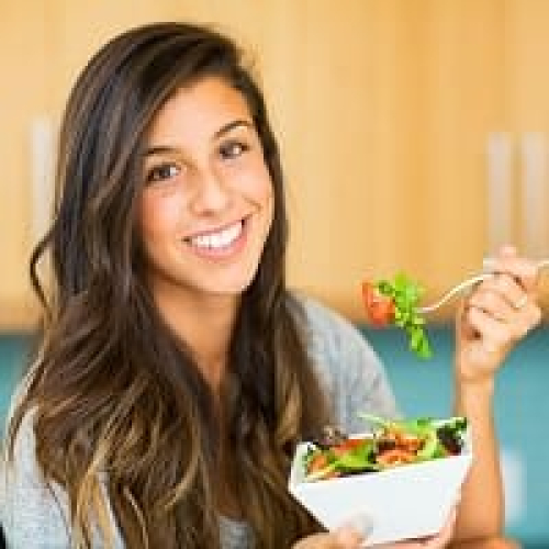 Smiling woman eating healthy salad for wellness and nutrition.