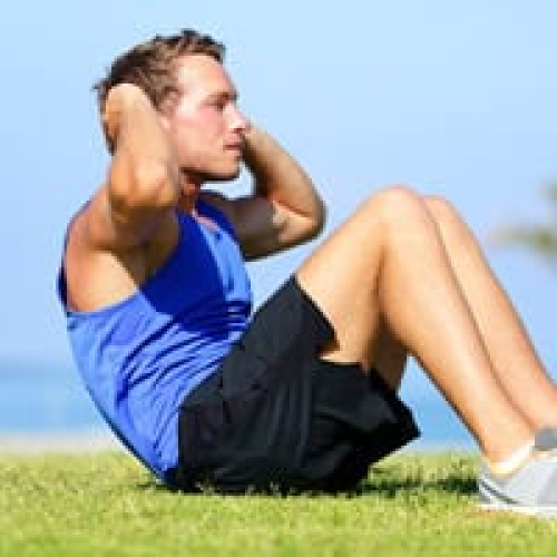 Young man exercising outdoors on grass with a blue sky background.